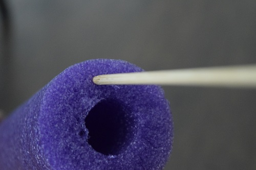 A skewer going into the bottom of a purple pool noodle.