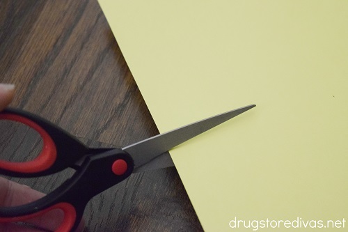 Scissors cutting a piece of yellow card stock.