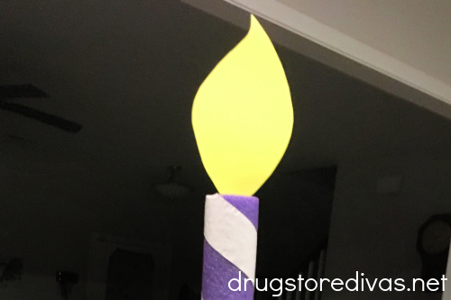 A yellow card stock flame coming out of the top of a purple and white pool noodle birthday candle.