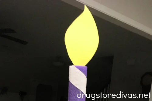 A yellow card stock flame coming out of the top of a purple and white pool noodle birthday candle.