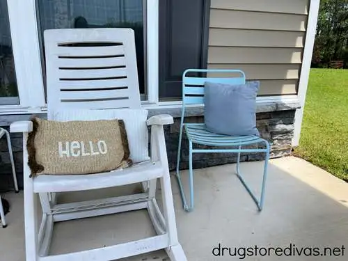 A white patio chair with a tan pillow and a blue patio chair with a darker blue pillow on a patio.