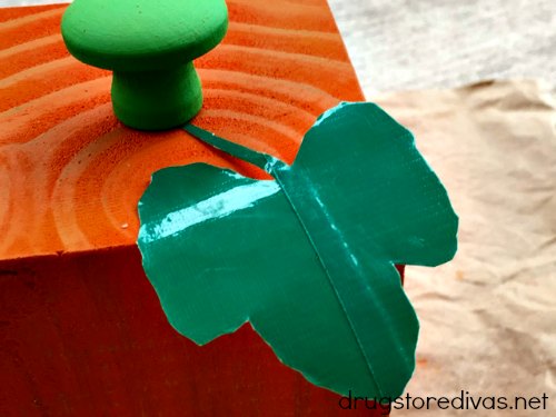 Duct tape leave and wooden drawer pull on top of an orange wooden pumpkin.