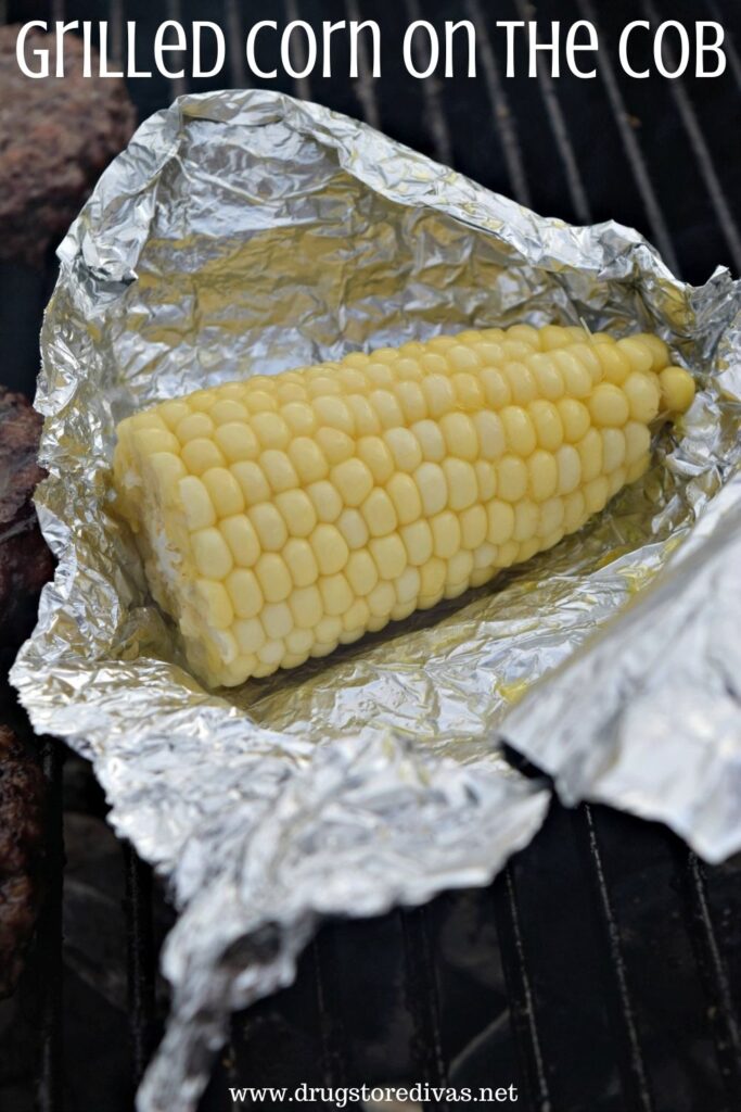 A piece of corn in an unwrapped piece of foil on the grill with the words "Grilled Corn On The Cob" digitally written on top.