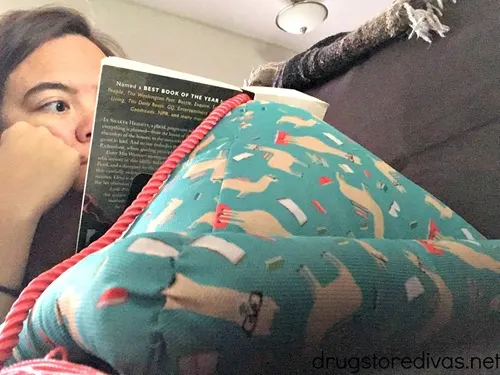 A woman reading a book that's leaning on a triangle book holder that's decorated with a llama fabric.