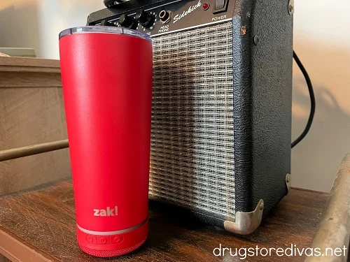 A red travel mug in front of a small speaker.