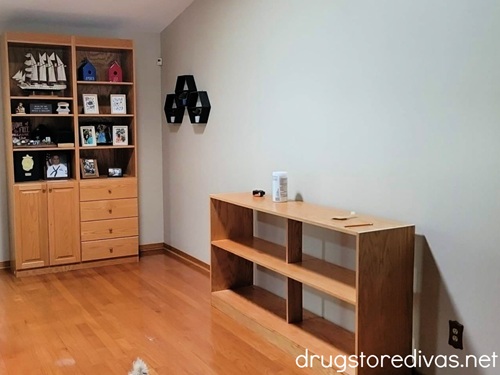 A living room with a filled bookcase, a long empty bookcase, and three shadow boxes on the wall.