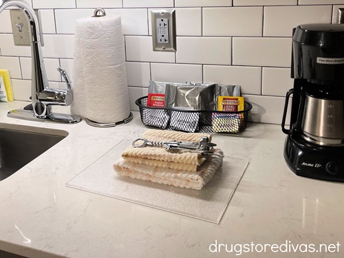 A kitchen with a pile of dish rags and a cork screw in the middle with a coffee maker, tea, and paper towels behind them and a sink off to the side.