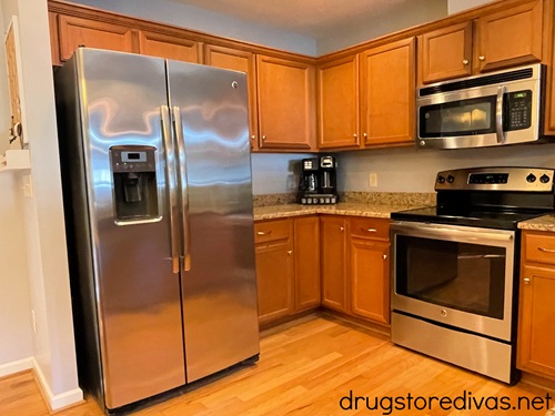 A full kitchen in a house, showing a fridge, cabinets, oven and microwave.