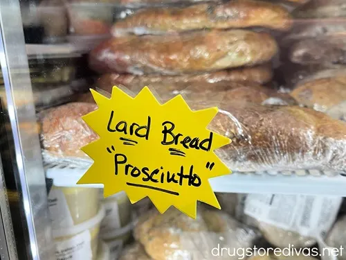 Bread on a shelf in a cooler with a large yellow piece of poster board on the front that says "Lard Bread Prosciutto" on it.