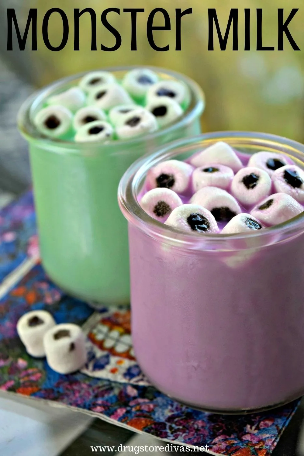 A cup of green milk with homemade marshmallow eyeballs and a cup of green milk with homemade marshmallow eyeballs on a napkin.