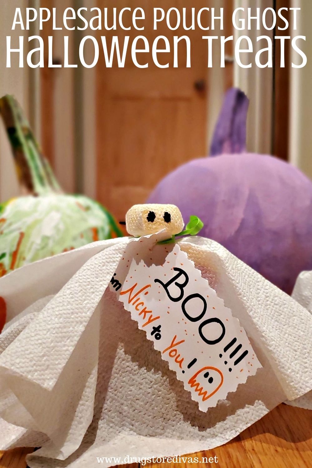 A napkin ghost in front of a green and a purple pumpkin with the words "Applesauce Pouch Ghost Halloween Treats" digitally written on top.