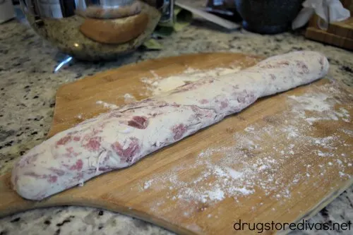 Prosciutto bread dough, rolled into a log shape, on a wooden pizza peel.