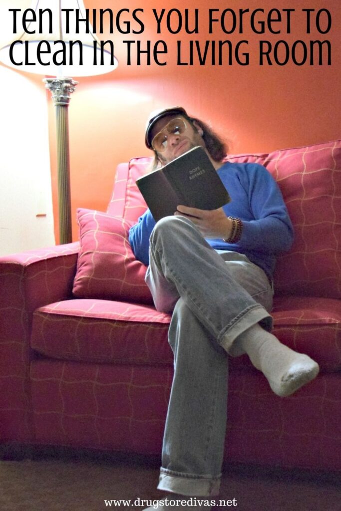 A man sitting on a couch reading a book, next to a lamp with the  words "Ten Things You Forget To Clean In The Living Room" digitally written above him.