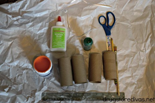 Supplies to make a DIY Toilet Paper Roll Pumpkin, including orange and green paint, glue, scissors, a pencil, a paint brush, a ruler, and toilet paper rolls.
