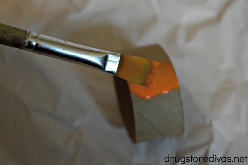 Paint brush painting a piece of toilet paper roll orange.