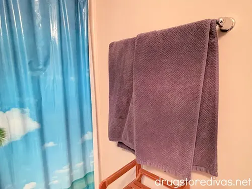 Blue bath towels on a rack next to a shower curtain with an image of a sky on it.