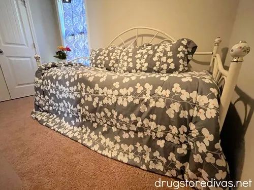 A bedroom with a bed with gray sheets with white flowers on it.