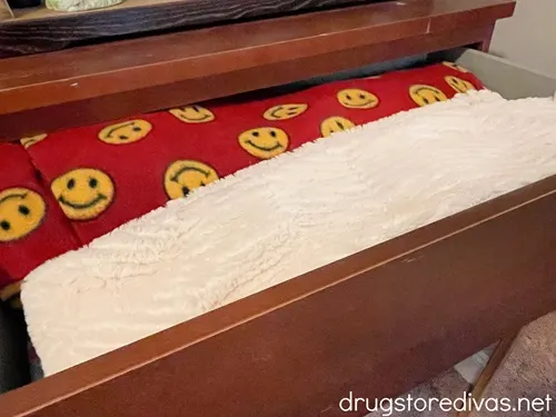 A red blanket with yellow smiley faces and a white blanket in a dresser drawer.