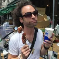 Man eating squid on a stick and a beer in a fish market in Japan with the words 