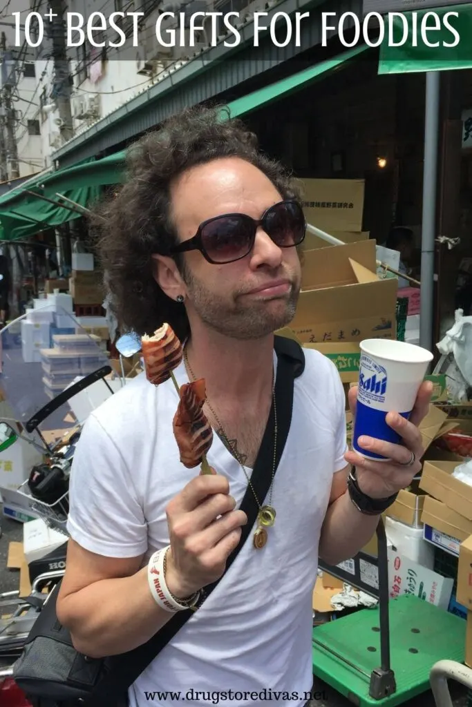 Man eating squid on a stick and a beer in a fish market in Japan with the words "10+ Best Gifts For Foodies" digitally written on top.