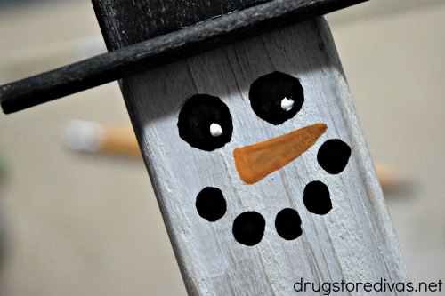 The face of a snowman painted on scrap wood.