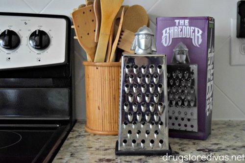 A cheese shredded, bamboo cooking tools, and a box next to an oven.