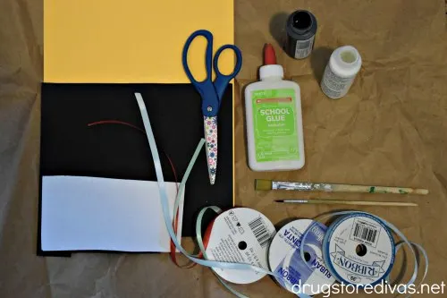Orange, black, and white cardstock, scissors, glue, black and white paint, a paint brush, and three rolls of ribbon.