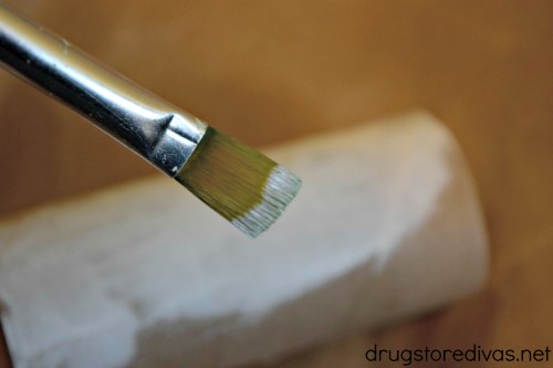 A paint brush painting a cardboard tube white.