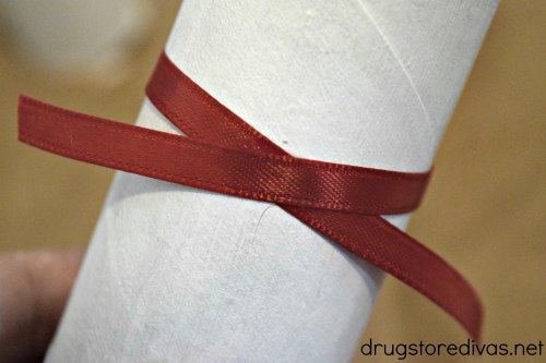 A maroon ribbon around a white cardboard tube.