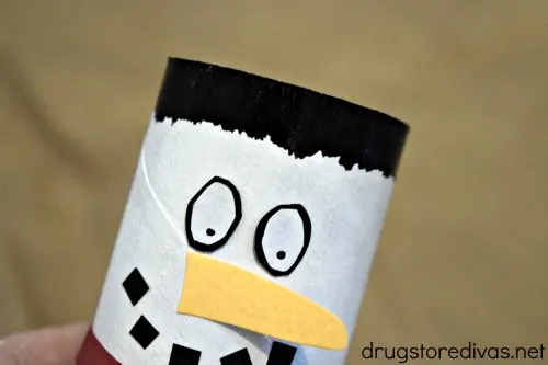 A snowman face and hair on a white cardboard tube.