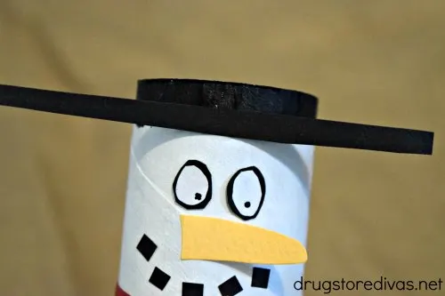 A snowman face and a top hat on a white card board tube.