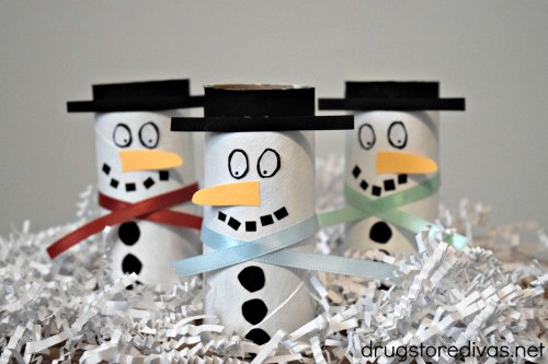 Three toilet paper roll snowmen standing in white paper shred.
