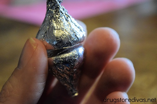A hand holding two silver Hershey's Kisses.