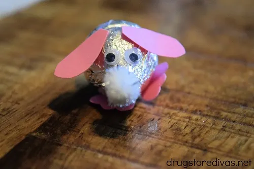 A pom pom nose, googly eyes, pink ears, and feet glued onto two silver Hershey's Kisses to look like a mouse.