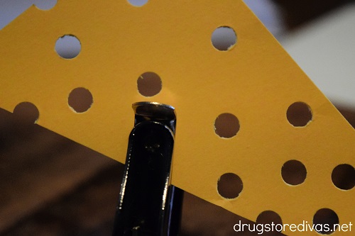 A hole puncher punching holes in a mustard colored piece of card stock.
