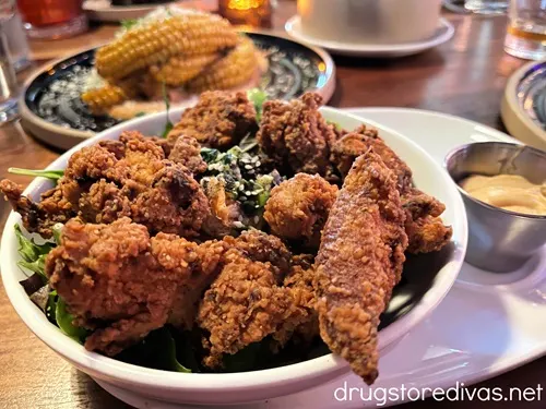 Chicken fingers on a bed of lettuce with curled corn behind it from True Blue Butcher & Barrel in Wilmington, NC.