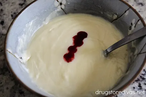 Red food coloring on top of melted white chocolate in a bowl with a spoon.