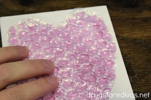 A bubble wrap heart painted pink being pushed down onto cardstock.