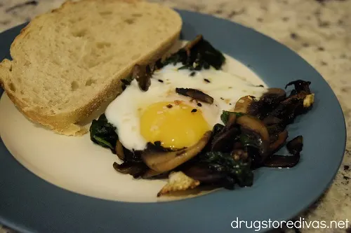 Egg In A Hole with mushrooms and spinach next to bread on a plate.