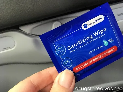 A sanitizing wipe being held up at an airline seat.
