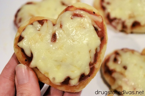 A hand holding a heart shaped pizza.