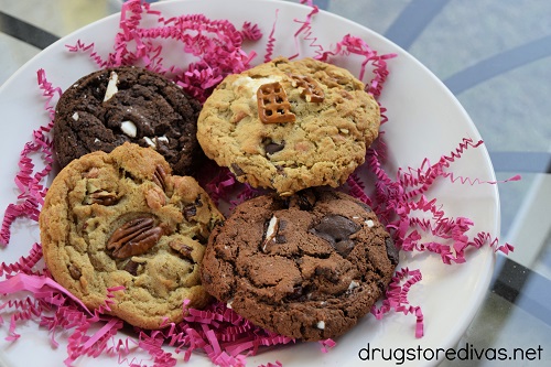 Four cookies on a plate with pink paper shred behind them.