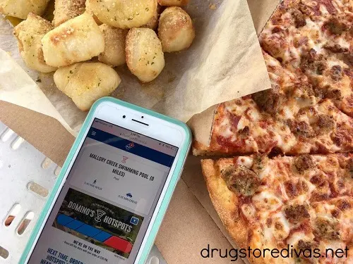 A phone showing a Dominos Hotspot, Dominos Pizza and garlic knots are nearby.