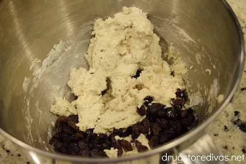 Bread dough and raisins in a stand mixer bowl.