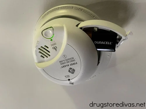 A smoke alarm attached to a ceiling in a home with the battery section open.