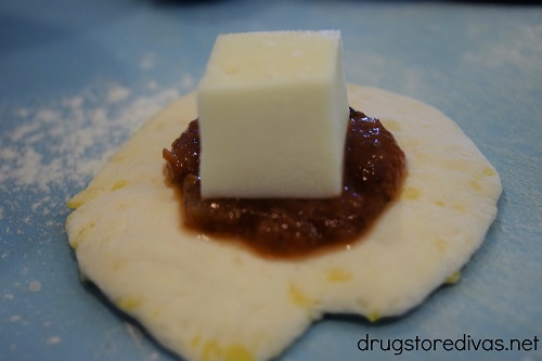 A dollop of marinara sauce and a square of cheese in a flattened piece of biscuit.