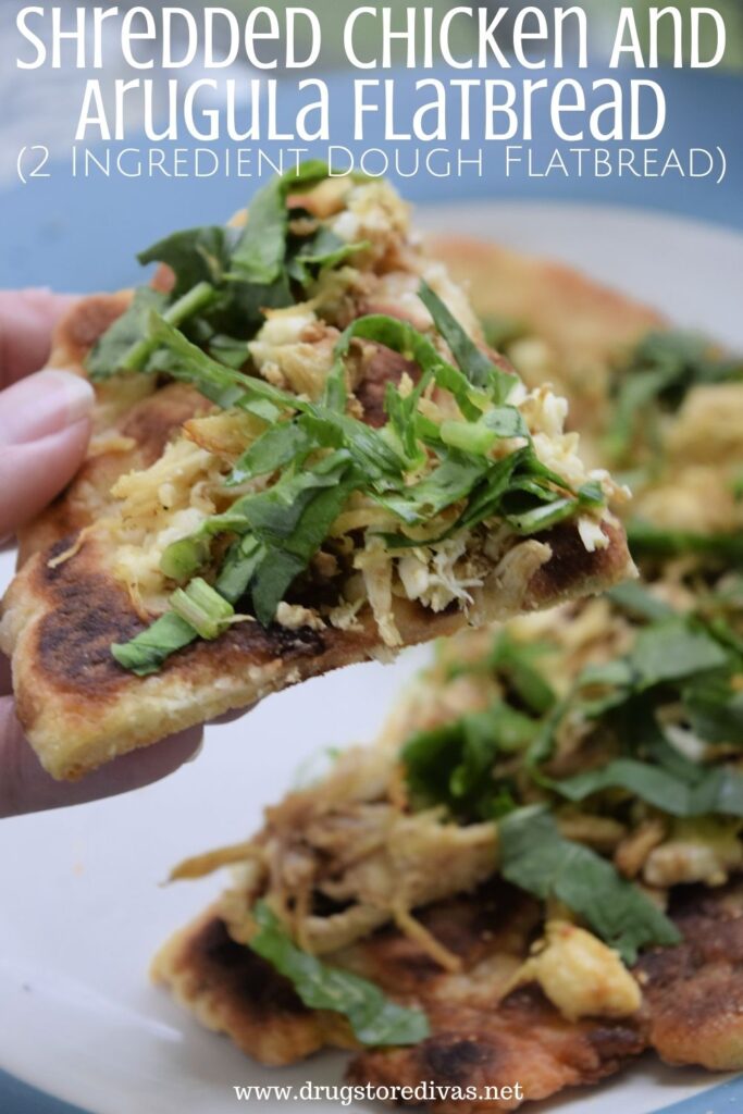 Fingers holding a piece of Shredded Chicken And Arugula Flatbread pizza above other pieces on a white plate with a blue trim.