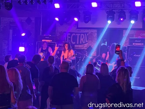 A band on stage with blue lights shining down and a crowd in front of them at Bowstring in Wilmington, NC.