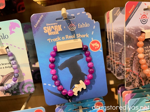 A purple beaded bracelet with a shark on it on a peg in a store.