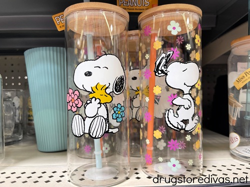 Two Snoopy glasses with lids and straws on a shelf in a store.